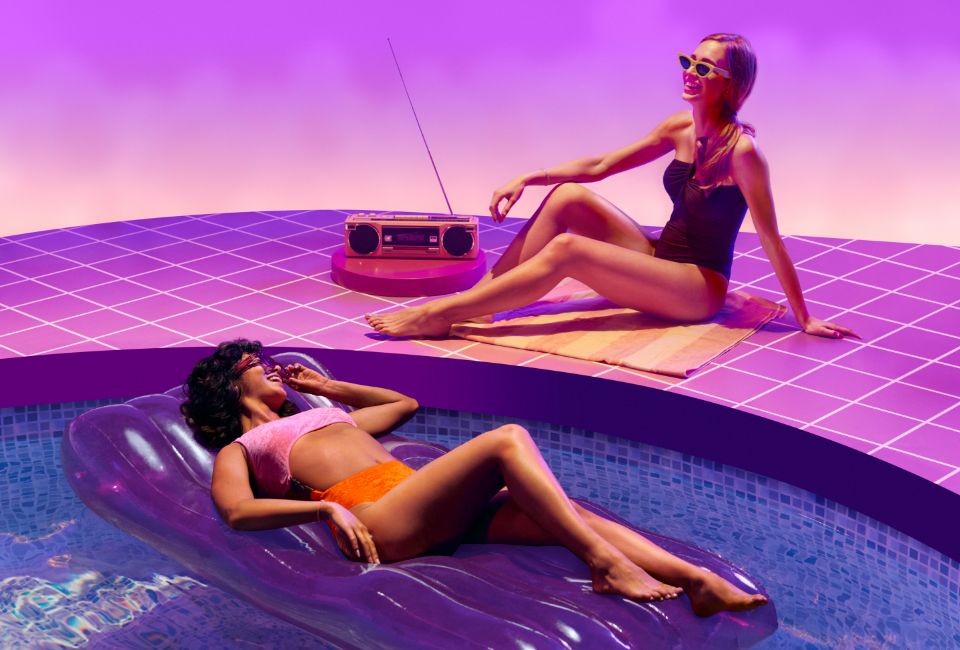 Two women in swimwear lounging at a pool listening to a stereo