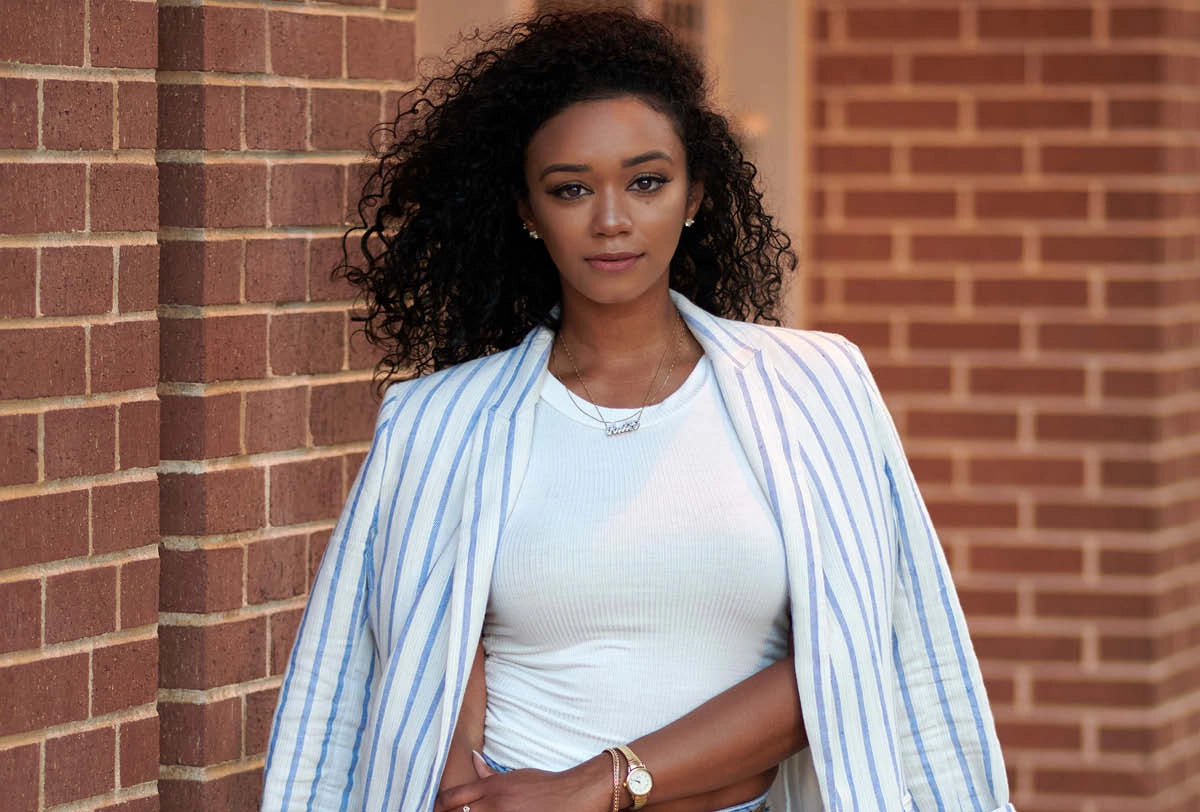 Woman wearing a light blue striped blazer over a white top against a brick wall.
