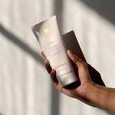 A woman's hand holding a tube of EWC SLOW Shea Body Polish.