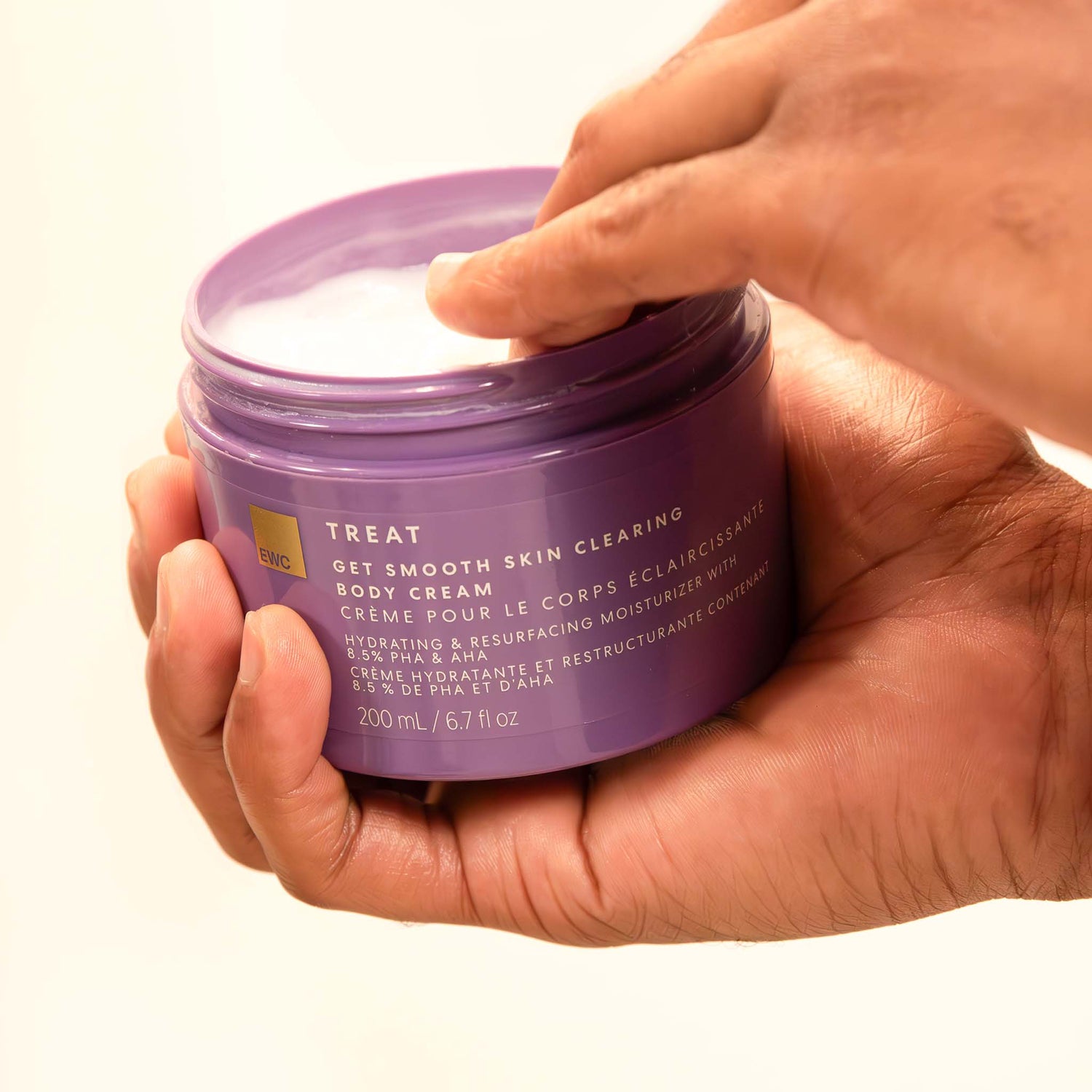 Hands holding an open tub of EWC TREAT Get Smooth Skin Clearing Body Cream.