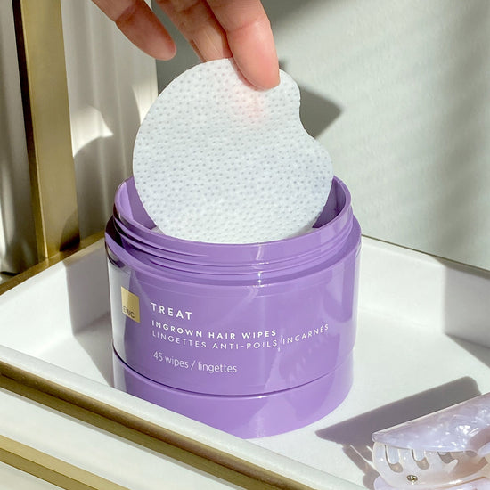 A hand pulls out a single wipe from a tub of EWC Treat Ingrown Hair Wipes.