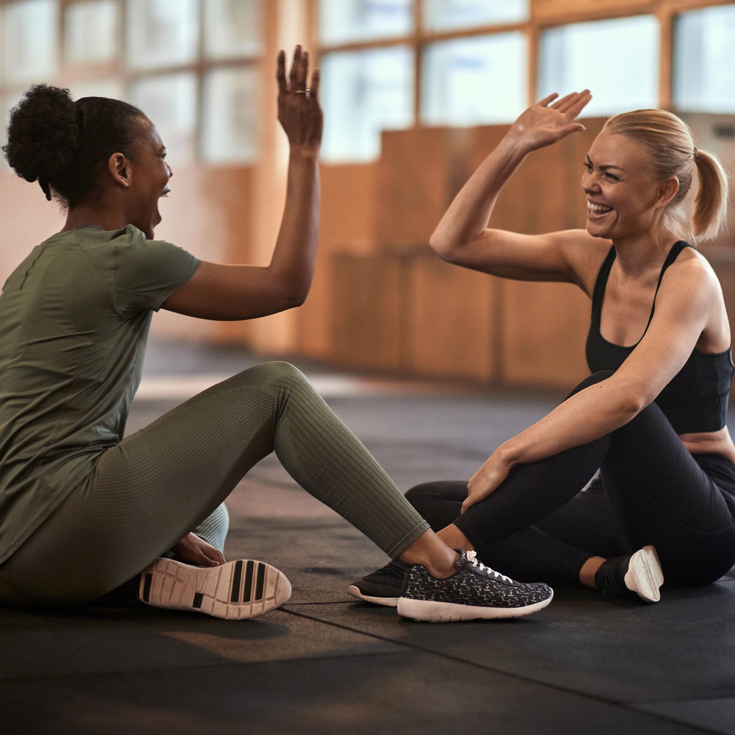 Two women high-fiving on a yoga mat in a gym setting