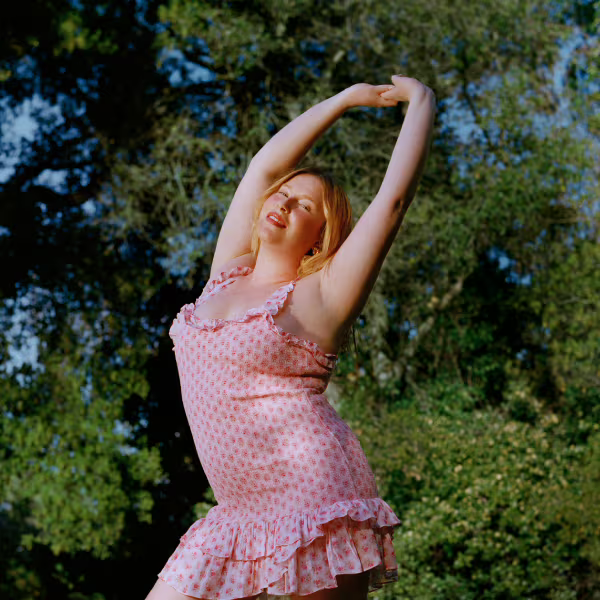 Woman in a pink dress in front of a tree with her arms in the air