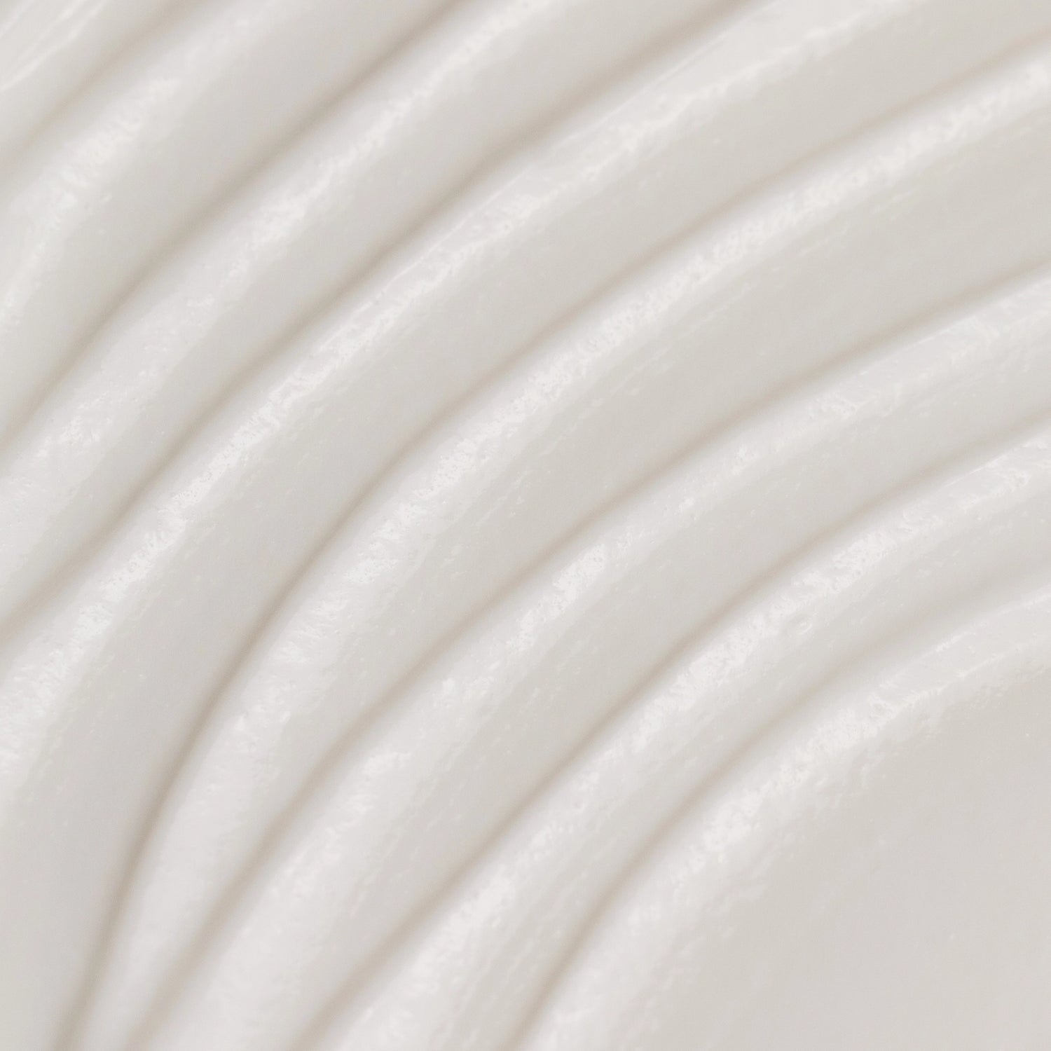 A close-up texture shot of a smooth, off-white cream or lotion with soft, curved ridges.