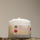 EWC Golden Orchard Body Butter against a cream background, styled against a rustic tree trunk.
