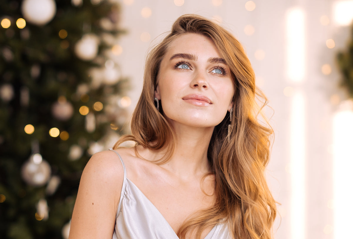 Woman with long blonde hair in a white dress against a festive background with lights and decorations.