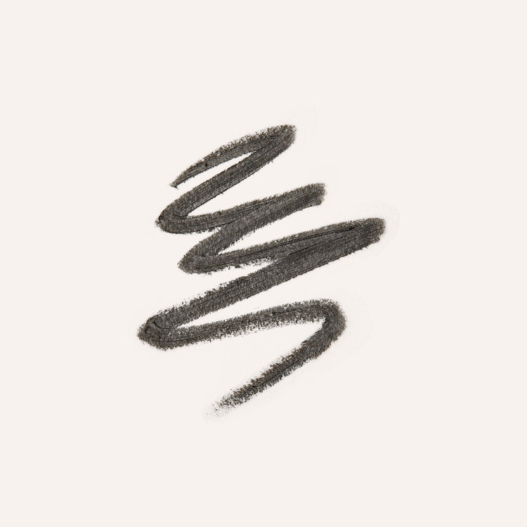 A textured swipe of dark brown eyebrow pencil on a solid off-white background.